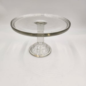 May include: A clear glass cake stand with a round base and a wide, flat top.