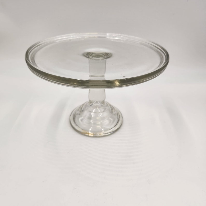 May include: A clear glass cake stand with a round base and a wide, flat top.
