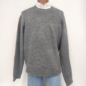 May include: A grey crew neck jumper made of a soft, knitted fabric.