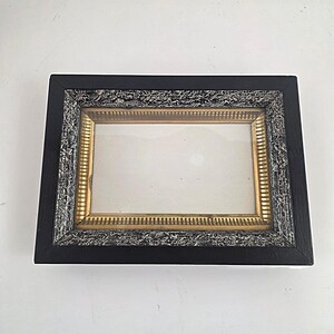 May include: A rectangular picture frame featuring a smooth black outer border, a textured silver-toned middle section with a distressed finish, and an inner gold-toned border with a repeating vertical line pattern surrounding a clear glass pane.