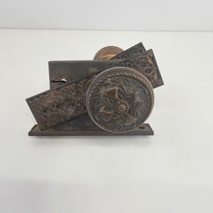 May include: Antique bronze door hardware set. The set includes two doorknobs with floral designs, a strike plate, and a keyhole cover. The hardware has an aged patina, with intricate details and a classic aesthetic.