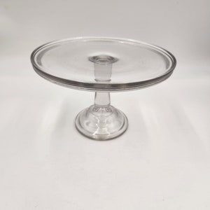 May include: A clear glass cake stand with a round base and a wide, flat top. The stand is perfect for displaying desserts or other treats.