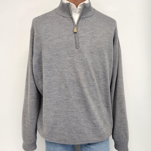 以下が含まれることがあります： グレーの長袖セーターで、1/4ジッパーが付いています。セーターはリブ編みの襟と袖口が付いています。