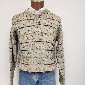 May include: A striped sweater with a speckled pattern in shades of brown, beige, red, and blue. The sweater has a button at the neck.