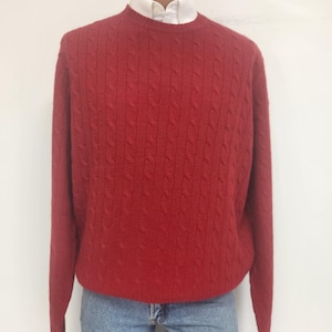 May include: A red cable knit jumper with long sleeves and a crew neck.