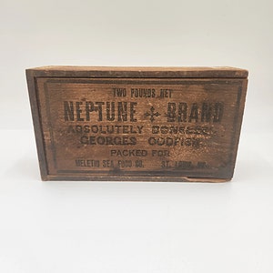 Könnte beinhalten: Eine Holzkiste mit einem Etikett, auf dem steht: "TWO POUNDS NET NEPTUNE + BRAND ABSOLUTELY BONELESS GEORGES CODFISH PACKED FOR MELETIO SEA FOOD CO. ST. LOUIS, MO."