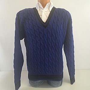 May include: A long-sleeved V-neck jumper in a vibrant blue cable knit pattern. The garment features a dark navy blue trim along the neckline, cuffs, and bottom hem. A crisp white collared shirt is visible underneath the jumper's neckline.