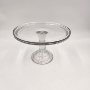 May include: A clear glass cake stand with a round base and a wide, flat top.