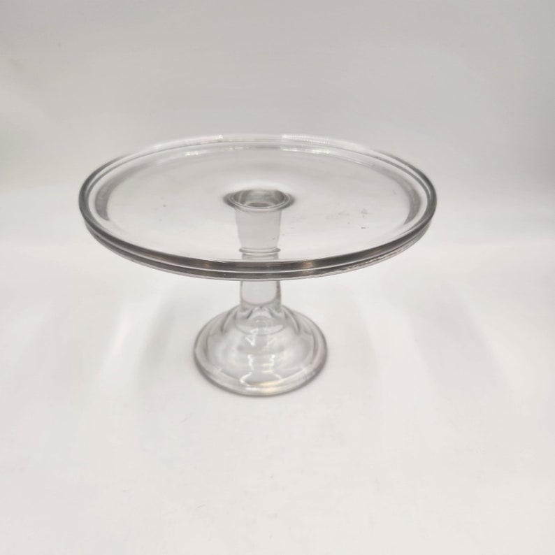 May include: A clear glass cake stand with a round base and a wide, flat top.