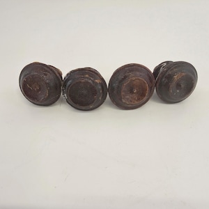 May include: Four dark brown, wooden cabinet knobs with a circular design. The knobs have a slightly domed top and a flat base. The wood grain is visible, and the knobs appear to be vintage or antique.