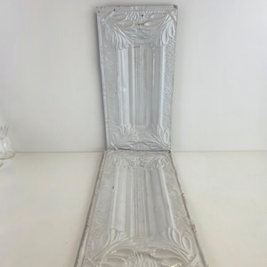 Puede incluir: Dos paneles decorativos rectangulares de metal blanco con diseños en relieve florales y geométricos ornamentados. Los paneles están articulados y el diseño incluye un panel vertical central con una serie de líneas verticales.
