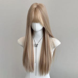 以下が含まれることがあります： マネキンの頭に展示された、まっすぐな前髪の長い明るいブロンドのかつら。 かつらは、ブロンドトーンの自然なブレンドを特徴としています。 シルバーの蝶のペンダントネックレスがマネキンの首からぶら下がっています。