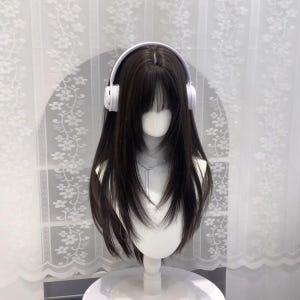 以下が含まれることがあります： 白いヘッドホンをつけた、長い黒髪と前髪のマネキンの頭。シルバーのネックレスが見えます。マネキンは白いスタンドの上にあり、白い花柄のカーテンを背景にしています。
