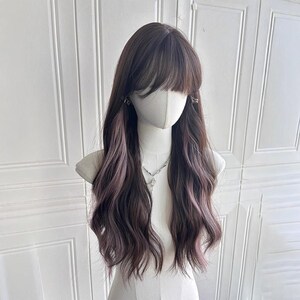 以下が含まれることがあります： 暗い茶色の髪と微妙なピンクのハイライトが入った、長く波打つウィッグ。ウィッグはフルフリンジで、マネキンの頭にスタイルされています。シルバーのネックレスが見えます。
