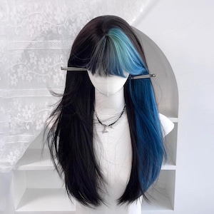 May include: A black wig with a blue and teal highlight, styled with long layers and bangs. The wig is displayed on a mannequin head with a silver necklace and hair clips.