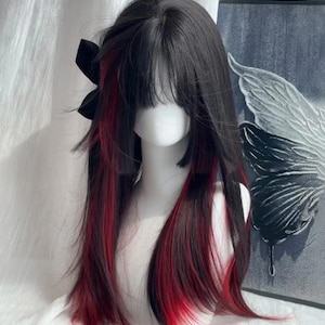 以下が含まれることがあります： 長いストレートヘアと鈍い前髪の黒いウィッグ。ウィッグは鮮やかな赤いストリークが特徴で、黒いリボンでスタイリングされています。ウィッグは白いマネキンの頭に表示されています。