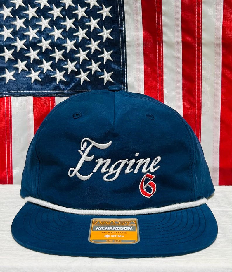 May include: A navy blue baseball cap with the word "Engine" embroidered in white script and the number "6" in red. The cap has a white rope detail and a flat brim. The Richardson brand tag is visible.