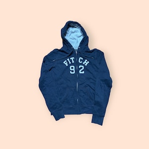 May include: Navy blue zip-up hoodie with a hood and white text that reads "FITCH 92". The interior of the hood is light gray. The hoodie has a full zipper and ribbed cuffs and hem.