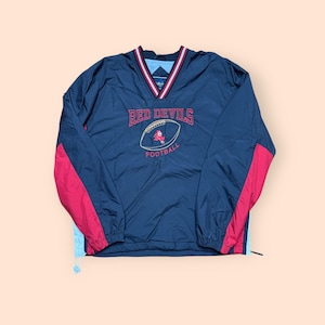 May include: A navy blue windbreaker jacket with red and light blue accents. The jacket has a v-neck and features an embroidered logo that says "Red Devils Football".