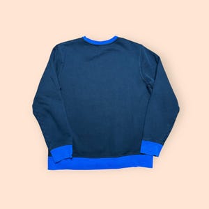 Puede incluir: Una sudadera azul marino con cuello redondo y mangas largas. El cuello y los pu&ntilde;os son de color azul brillante. La sudadera est&aacute; hecha de un material suave y es probablemente para uso casual.