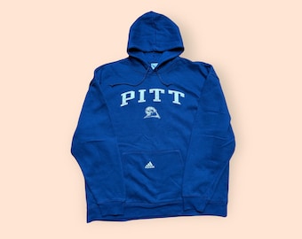 May include: A blue hooded sweatshirt with the word "PITT" in white lettering and a small logo on the front. The sweatshirt has a kangaroo pocket and a white Adidas logo on the pocket.