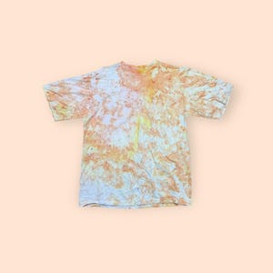 May include: A tie-dye t-shirt with a white base and orange and yellow dye. The dye is unevenly distributed, creating a marbled effect.