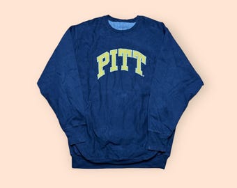 May include: Navy blue sweatshirt with the word "PITT" in yellow block letters across the chest. The sweatshirt has long sleeves and a crew neck. The fabric appears to be a soft, worn material.