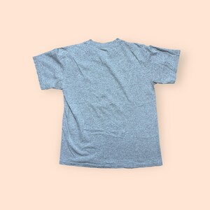 May include: A heather gray short-sleeved t-shirt. The shirt is made of a soft, textured fabric and has a crew neck. The t-shirt is laid flat on a light orange background.