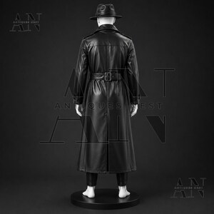 K&ouml;nnte beinhalten: Ein schwarzer Ledertrenchcoat mit passendem G&uuml;rtel und breitem Kragen, getragen &uuml;ber einer dunklen Hose. Der Mantel hat eine lange, strukturierte Silhouette mit einem mittigen R&uuml;ckenschlitz. Ein schwarzer Fedora-Hut wird von der wei&szlig;en Schaufensterpuppe getragen.