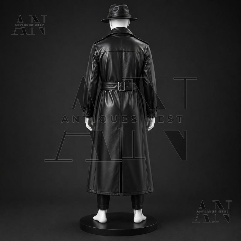 K&ouml;nnte beinhalten: Ein schwarzer Ledertrenchcoat mit passendem G&uuml;rtel und breitem Kragen, getragen &uuml;ber einer dunklen Hose. Der Mantel hat eine lange, strukturierte Silhouette mit einem mittigen R&uuml;ckenschlitz. Ein schwarzer Fedora-Hut wird von der wei&szlig;en Schaufensterpuppe getragen.