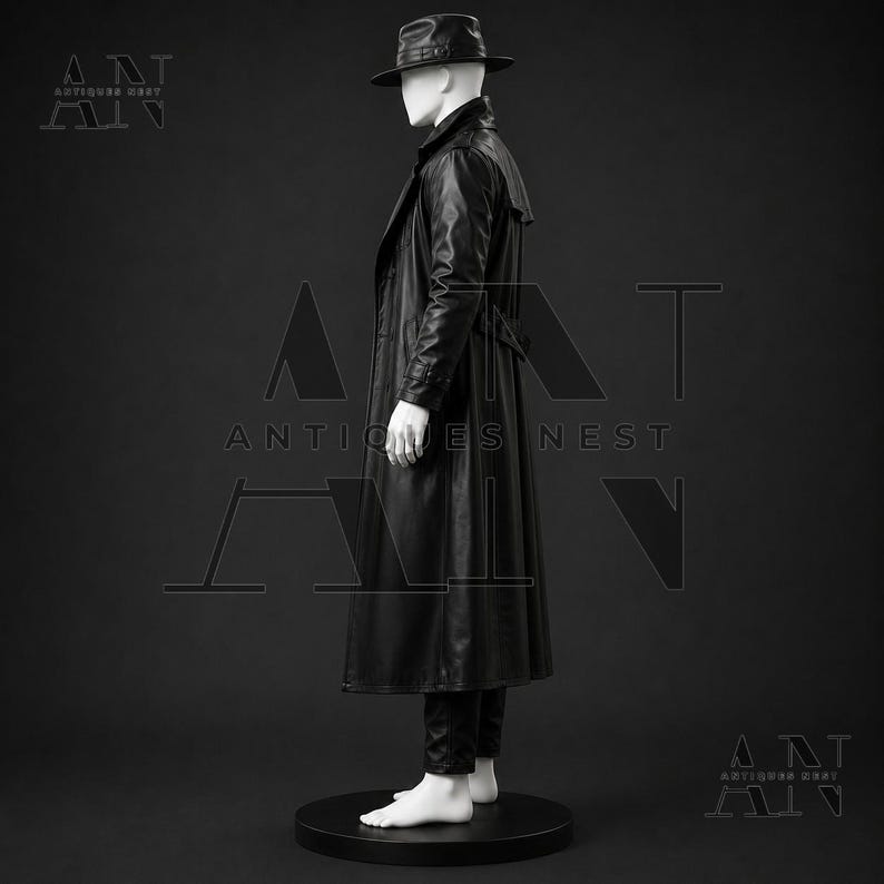 K&ouml;nnte beinhalten: Ein schwarzer Ledertrenchcoat an einer wei&szlig;en Schaufensterpuppe. Die Puppe tr&auml;gt zudem einen schwarzen Fedora-Hut und eine schwarze Hose. Das Ensemble steht auf einem runden schwarzen Sockel. Der Text Antiques Nest ist im Hintergrund zu sehen.