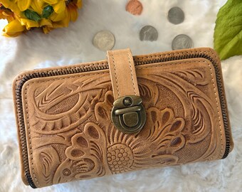 Puede incluir: Una cartera de cuero marrón con un diseño floral en relieve y un cierre de metal. La cartera tiene una cremallera y está hecha de cuero de alta calidad.
