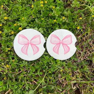 May include: Two white round coasters with a pink bow design.