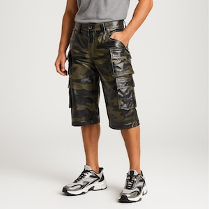 Può includere: Pantaloncini cargo con stampa mimetica nei toni del verde e del nero. I pantaloncini presentano più tasche e una texture simile alla pelle. Il modello indossa sneakers nere e argento.