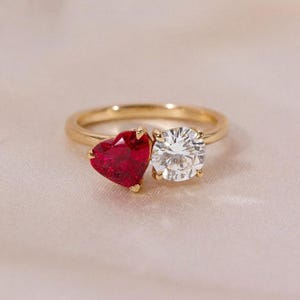 May include: A gold ring with a heart-shaped ruby and a round diamond. The ruby is red and the diamond is clear.