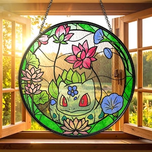 Puede incluir: Ventana redonda de vidrieras con un personaje de Bulbasaur rodeado de flores rosas y azules y hojas verdes. La ventana está enmarcada en negro y cuelga de una cadena. El fondo muestra una ventana abierta con un día soleado.