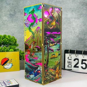 Puede incluir: Lámpara rectangular con marco de madera, que muestra ilustraciones coloridas de criaturas al estilo japonés. La lámpara emite un brillo rosa. La obra de arte incluye un dragón verde, una criatura roja y blanca y otros personajes.