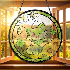 Puede incluir: Vidriera redonda que representa un gato de dibujos animados con pelaje verde y blanco, un ojo rosa y la lengua fuera. El diseño incluye girasoles, tréboles y una mariposa. La ventana está colgada frente a una ventana abierta.