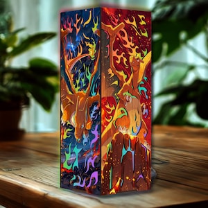Puede incluir: Lámpara rectangular de madera con una ilustración de Charizard. La obra de arte muestra al Pokémon sobre un fondo de llamas y un paisaje de fuego. La paleta de colores incluye tonos de naranja, rojo, azul y amarillo. Artículo decorativo.