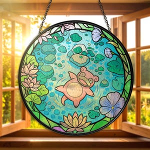 Puede incluir: Una vidriera redonda que presenta un personaje de dibujos animados Slowpoke flotando en un estanque. El diseño incluye nenúfares, hojas de nenúfar y flores azules y moradas, con un marco de metal negro y una cadena para colgar.