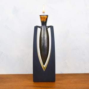 May include: A black ceramic candle holder with a gold trim. The candle holder is shaped like a vase and has a narrow opening at the top. A lit candle is inside the holder.