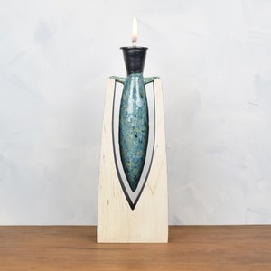 May include: A teal blue ceramic oil lamp with a black top and a flame, sitting on a wooden stand.