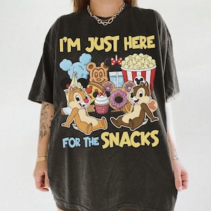 Puede incluir: Camiseta gris oscuro con el texto "I'M JUST HERE FOR THE SNACKS" en amarillo y azul. El gráfico presenta a Chip y Chop con varios snacks como palomitas de maíz, donuts y helado.