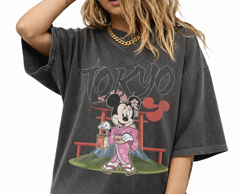 Peut inclure: T-shirt gris fonc&eacute; surdimensionn&eacute; avec un motif de Minnie Mouse en kimono rose, tenant une lanterne, avec le mot "Tokyo" au-dessus. Le design comprend des &eacute;l&eacute;ments japonais et un torii rouge.