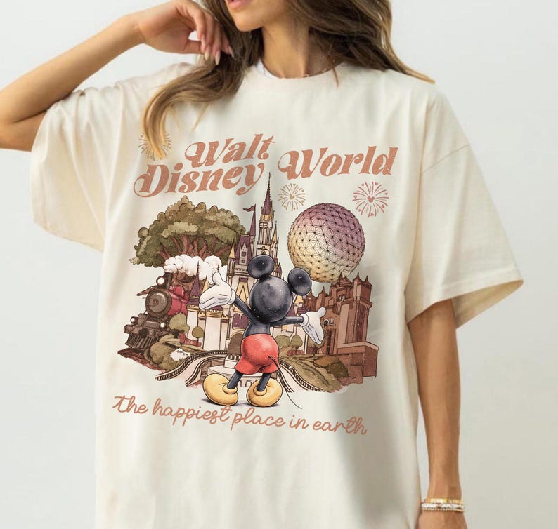 May include: Cream-colored t-shirt featuring a graphic of Mickey Mouse in front of a Disney World scene. The design includes a train, castle, and Spaceship Earth, with the text "Walt Disney World" and "The happiest place in earth".