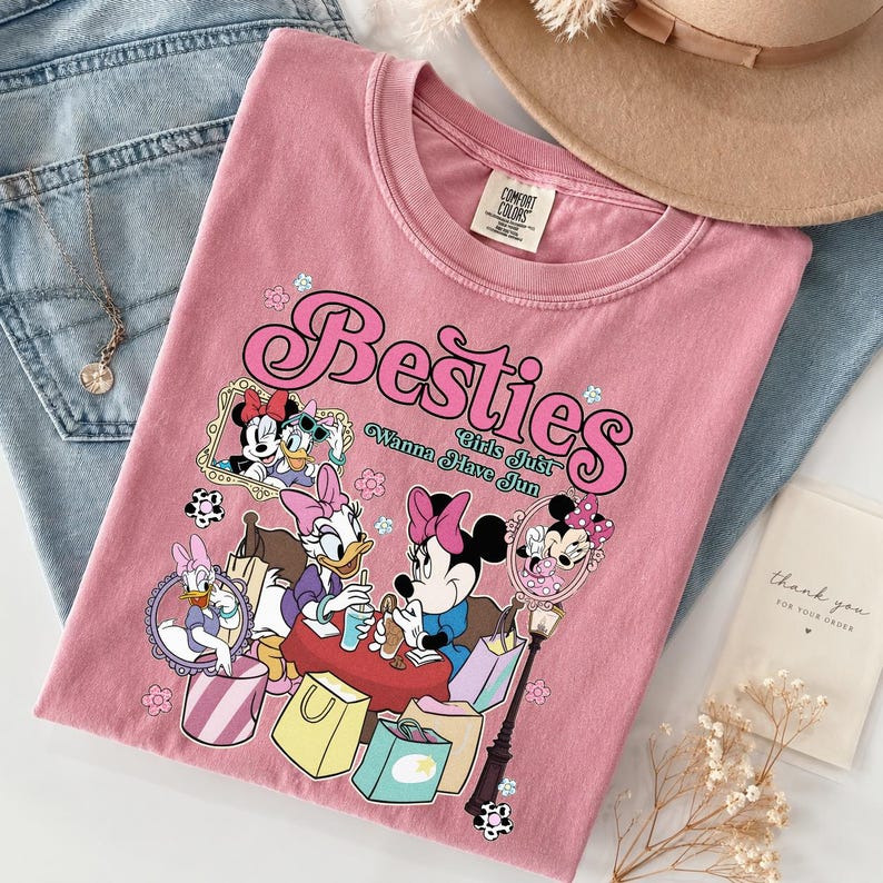 May include: Pink t-shirt with a graphic of Minnie Mouse, Daisy Duck, and other Disney characters. The shirt has the word "Besties" in a bubble font, with the phrase "Girls Just Wanna Have Fun".