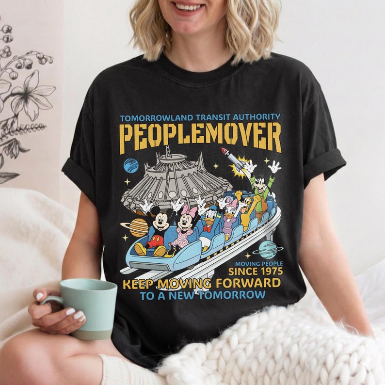 May include: Black t-shirt featuring a colorful graphic of the PeopleMover ride with Mickey, Minnie, Donald, and Goofy. The shirt has the text "TOMORROWLAND TRANSIT AUTHORITY PEOPLEMOVER" and "KEEP MOVING FORWARD TO A NEW TOMORROW."