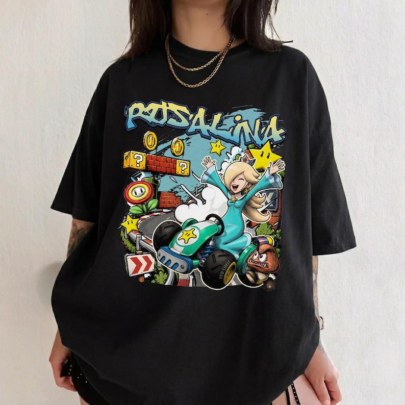 May include: Black t-shirt featuring a colorful graphic of Rosalina from Mario Kart. The design includes a kart, stars, coins, and the word "Rosalina" in graffiti-style lettering. The shirt is oversized.