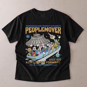 May include: Black t-shirt featuring a colorful graphic of the PeopleMover ride with Mickey Mouse, Minnie Mouse, Donald Duck, and other characters. The shirt includes the text "Tomorrowland Transit Authority PEOPLEMOVER" and "Moving People Since 1975."