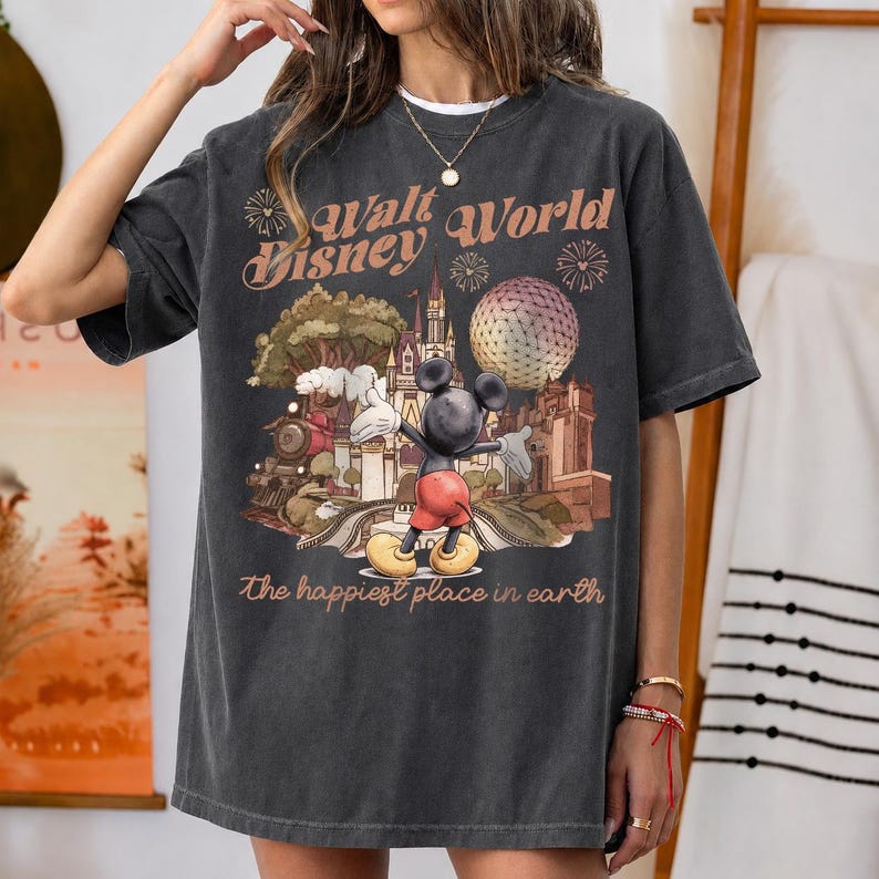 May include: Dark gray t-shirt featuring a vintage-style graphic of Mickey Mouse in front of a castle, a golf ball-shaped structure, and the text "Walt Disney World." The phrase "The happiest place in earth" is printed below the graphic.